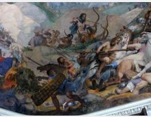 Affresco storico con scena di battaglia ambientata in un paesaggio roccioso e collinare, con grandi massi, vegetazione bassa e alberi sullo sfondo. La composizione è dinamica e ricca di armi, cavalli e figure in movimento, tipica di una decorazione murale monumentale.