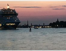 Grande nave da crociera illuminata sul lato sinistro che naviga in un ampio canale al crepuscolo. Sullo sfondo si vede una skyline di edifici e campanili lungo la riva, con luci cittadine e cielo rosato.