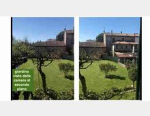 Vista dall’alto su un giardino con prato verde, alberi potati e siepi, delimitato da un muro in pietra. Sullo sfondo si vedono edifici in muratura con tetti in coppi rossi e un portico con copertura.