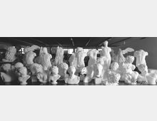 Interno di un laboratorio o magazzino d’arte con numerose statue e busti bianchi in gesso o marmo disposti su tavoli e piedistalli. L’ambiente ha soffitto industriale e finestre sullo sfondo che illuminano le sculture classiche.