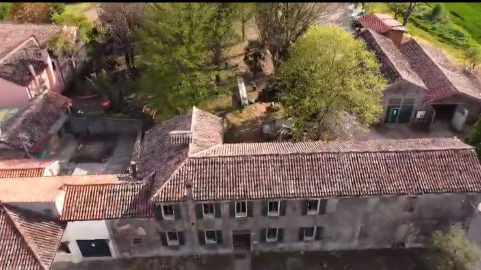 Veduta aerea di un complesso rurale con lunghi edifici in muratura dai tetti in tegole rosse e cortili interni. Intorno si vedono alberi e aree verdi che circondano le costruzioni.
