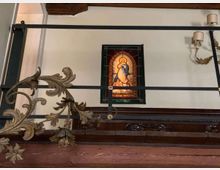 Interno con soppalco e ringhiera in metallo decorata, soffitto con travi in legno e pareti chiare. Al centro è visibile una vetrata colorata in stile religioso incorniciata, con applique a parete sulla destra.