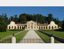 Villa storica in stile neoclassico con corpo centrale e ali porticate ad archi, vista frontalmente lungo un viale rettilineo che attraversa un ampio prato. In primo piano si vede una recinzione in ferro e sullo sfondo un’area alberata.