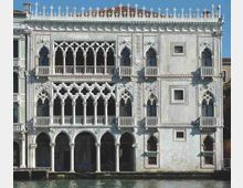 Facciata di un palazzo storico in pietra chiara affacciato su un canale, con portico ad archi al piano terra e logge gotiche ai piani superiori con trafori e balconate. Il coronamento presenta una merlatura decorativa lungo il tetto sotto un cielo sereno.
