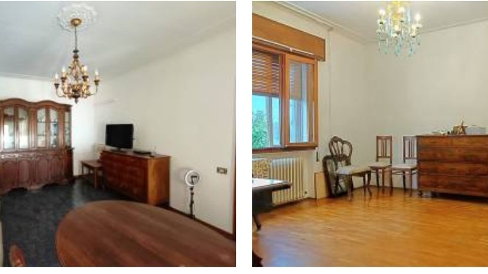 Interno di un’abitazione con due stanze: un soggiorno con divani, tavolo ovale, grande credenza in legno, TV su mobile e lampadario a chandelier. Seconda stanza con parquet, finestra con tapparella, termosifone, cassettiera e sedie lungo la parete, con piccolo lampadario al soffitto.